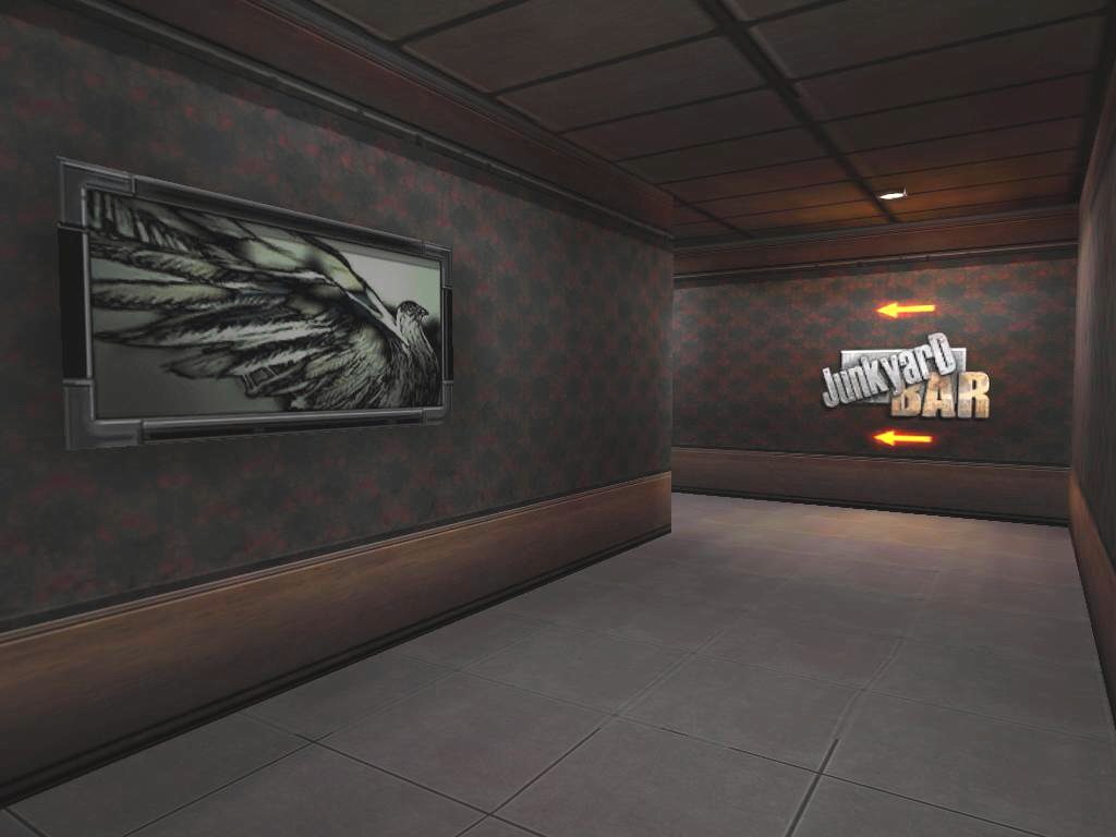 A dimly lit corridor leading to the Junkyard Bar, featuring dark patterned wallpaper, a framed artwork of a bird's wing on the left, and a sign for the Junkyard Bar with arrows on the right.