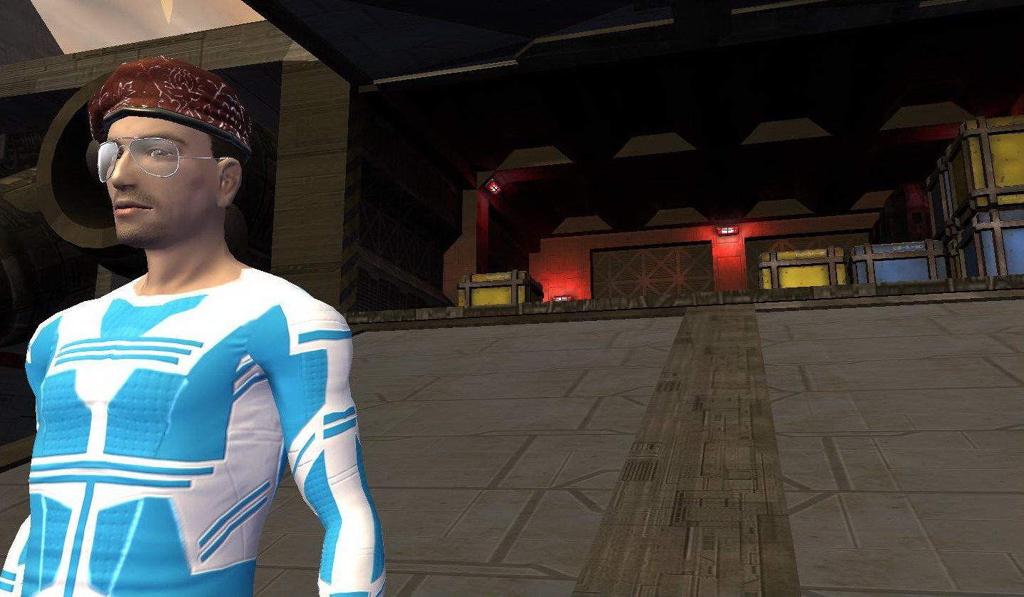 A male avatar in a blue and white outfit and red beret stands on a metallic platform. Behind him are colorful crates and red lights in a dimly lit industrial setting.